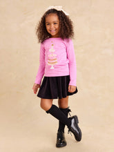 Load image into Gallery viewer, A young girl with curly brown hair wearing a pink long-sleeve top with a cake graphic, a black velvet skirt, black knee-high socks, and black shoes, standing against a beige textured background.
