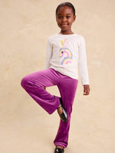 Load image into Gallery viewer, A young girl modeling a white long-sleeve t-shirt with a pastel rainbow graphic and bright purple velvet pants, standing against a textured beige background.
