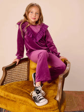 Load image into Gallery viewer, Young girl in a purple outfit sitting on a yellow chair against a beige wall.
