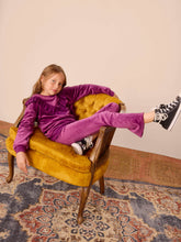 Load image into Gallery viewer, Child in purple outfit sitting on a yellow armchair with a patterned rug below
