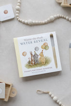 Load image into Gallery viewer, Pooh’s Birthday Surprise water reveal book displayed on a tabletop beside wooden beads, with the water pen alongside.
