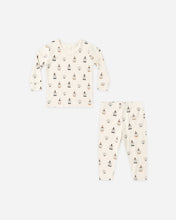 Load image into Gallery viewer, A two-piece baby pajama set featuring a long-sleeve top and matching pants in an off-white/cream color, both printed with a small repeating pattern of Christmas trees, snowmen, and snowflakes.
