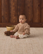 Load image into Gallery viewer, Baby sitting barefoot in cream rocking-horse print pants and a tan chunky knit sweater beside pine cones.
