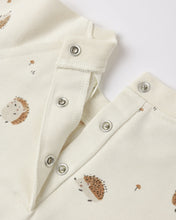 Load image into Gallery viewer, Close-up of a cream-colored baby garment with a hedgehog print and silver metal snap buttons, laid flat on a white background.
