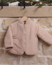 Load image into Gallery viewer, Rose water pink jacket hanging against a stone fireplace, showing the smooth side, front zipper, and shearling-lined collar.
