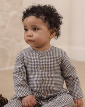 Load image into Gallery viewer, A baby with curly dark hair wearing a brown and beige gingham long-sleeve romper with brown buttons, sitting in a soft neutral indoor setting.
