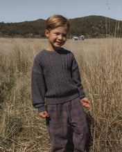 Load image into Gallery viewer, A young boy standing in a dry grassy field wearing a dark gray cable-knit sweater and plaid pants.
