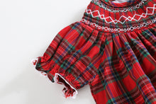 Load image into Gallery viewer, A close-up of a red plaid dress with white smocked detailing at the neckline and white ruffled trim at the sleeve cuffs, shown on a plain light background.
