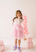 Load image into Gallery viewer, Child wearing a Sugar Plum dress with a long-sleeve holiday-print bodice and tiered pink tulle skirt beside pink gifts.
