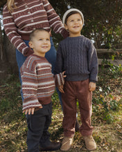 Load image into Gallery viewer, Three children outdoors wearing knit and corduroy sweaters and pants, with a woman partially visible behind them in a natural yard setting.
