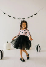 Load image into Gallery viewer, Child in Halloween-themed outfit with black tulle skirt and pink top with black cat pattern, standing in front of decorative pumpkins and bat banner.
