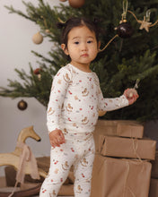 Load image into Gallery viewer, Child wearing cream Toy Chest print pajamas beside a decorated Christmas tree and brown paper-wrapped gifts.
