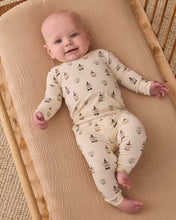 Load image into Gallery viewer, A baby lying on a muslin bassinet wearing a cream-colored long-sleeve footed sleeper with a small sailboat pattern.

