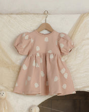Load image into Gallery viewer, A baby girl's dusty pink dress with white ghost prints, hanging on a wooden hanger against a textured cream fabric backdrop.
