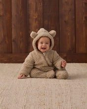 Load image into Gallery viewer, Baby crawling on a cream rug in a latte tan fleece jumpsuit with the bear-ear hood up.
