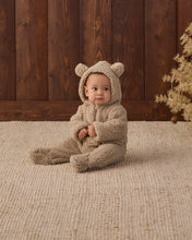 Load image into Gallery viewer, Baby sitting on a cream rug wearing a latte tan fleece jumpsuit with the bear-ear hood up.
