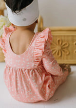 Load image into Gallery viewer, A child seen from behind wearing a pink long-sleeve romper with a white floral print and ruffled shoulder details, paired with a white headband, sitting indoors.
