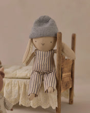 Load image into Gallery viewer, Ryder the Rabbit seated on a miniature wooden bed with cream bedding, wearing striped overalls and a gray beanie.
