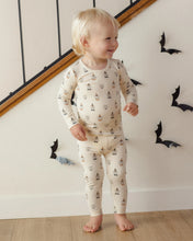 Load image into Gallery viewer, A toddler stands barefoot indoors wearing a cream long-sleeve pajama set with a repeating small boat print. The room has a light wall, wooden floor, and black bat decorations.
