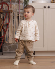 Load image into Gallery viewer, Toddler standing in a cream rocking-horse print shirt with latte tan drawstring pants and white socks.
