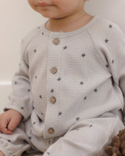 Load image into Gallery viewer, A close-up of a baby wearing a light gray waffle-knit romper with small dark gray star prints and four wooden buttons down the front.
