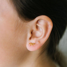 Load image into Gallery viewer, Close-up of a gold-tone bow stud earring worn on an earlobe, with hair pulled back.
