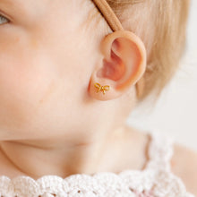 Load image into Gallery viewer, Close-up of a child wearing a gold-tone bow stud earring with delicate loops and short ribbon tails.
