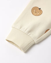 Load image into Gallery viewer, Close-up of a cream-colored sweatshirt sleeve featuring a cute embroidered pumpkin graphic with a smiling face and a ribbed cuff.
