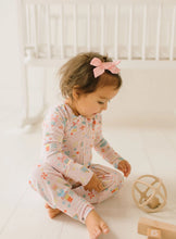 Load image into Gallery viewer, Side view of a seated baby in Sugar Plum zip pajamas, showing the front zipper, long sleeves, and open foot cuffs.
