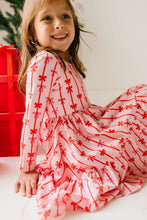 Load image into Gallery viewer, Close-up of a seated child wearing the Dainty Bows dress, showing the gathered waist, red bow print, and ruffled skirt.
