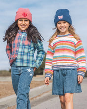 Load image into Gallery viewer, Two young girls walking outdoors on a paved path. The girl on the left wears a pink beanie with a smiley face, a blue and green plaid button-up shirt, and blue jeans with white star patches.
