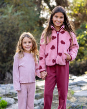 Load image into Gallery viewer, Two young girls standing outdoors holding hands, wearing matching knit loungewear. The girl on the right wears a pink fleece zip-up jacket with dark red heart patterns and dark pink pants, while the girl on the left wears a matching pink knit top and pants.
