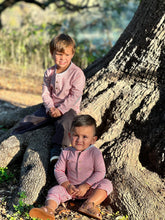 Load image into Gallery viewer, Two young boys wearing matching pink and white striped long-sleeve shirts and shorts sit outdoors on the base of a large tree trunk in warm sunlight.

