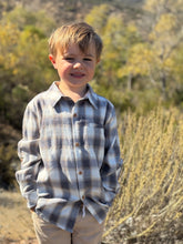 Load image into Gallery viewer, Young boy wearing a plaid shirt standing outdoors with trees in the background

