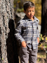 Load image into Gallery viewer, Child in plaid shirt and gray pants standing next to a tree in an outdoor setting
