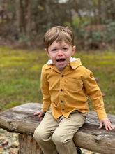 Load image into Gallery viewer, A young toddler boy wearing a mustard yellow long-sleeve button-up shirt and beige pants, sitting on a weathered log in an outdoor park setting.
