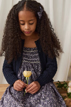 Load image into Gallery viewer, A young girl with long, curly dark hair wearing a navy blue cable-knit cardigan over a purple and white floral dress, holding a single pale yellow tulip.
