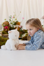Load image into Gallery viewer, Child lying beside Moon the Kitty plush, seated upright among moss and flowers.
