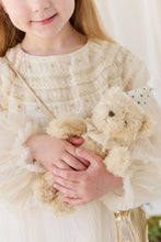 Load image into Gallery viewer, Child in a cream dress cradling Party Arthur teddy bear, with its gold-dotted hat and ribbon bow visible.
