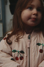 Load image into Gallery viewer, A close-up shot of a young girl wearing a light pink puffer jacket decorated with sequined cherry motifs.
