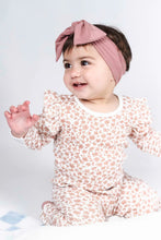 Load image into Gallery viewer, A baby girl wearing a long-sleeve footed pajama set with a small floral pattern in dusty pink and cream, paired with a matching dusty pink bow headband, sitting against a white studio background.

