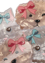 Load image into Gallery viewer, A close-up of several translucent plastic dog-shaped items, likely coasters or small accessories, decorated with printed dog faces and bows in pink, red, and light blue.
