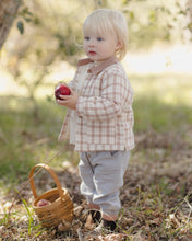 Load image into Gallery viewer, A toddler standing outdoors in a wooded setting, wearing a beige and white gingham button-up shirt and light gray pants, holding a red apple next to a small woven basket.
