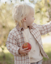 Load image into Gallery viewer, A toddler with blonde hair wearing a beige and brown plaid button-up jacket over a cream fleece shirt, holding a red apple in an outdoor garden setting.
