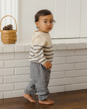 Load image into Gallery viewer, A toddler standing barefoot in front of a white brick wall, wearing a cream knit sweater with gray horizontal stripes and light gray pants.
