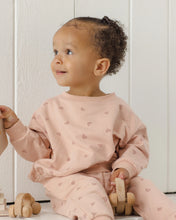 Load image into Gallery viewer, A toddler wearing a light pink long-sleeve sweatshirt and matching pants with a small heart pattern, sitting on a white wooden floor with wooden toys.
