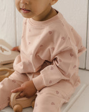 Load image into Gallery viewer, A baby wearing a light pink long-sleeve sweatshirt and matching pants set, both decorated with a small repeating heart pattern. The baby is sitting on a white surface next to a wooden toy car.
