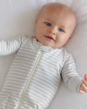 Load image into Gallery viewer, A baby lying on a white blanket wearing a long-sleeve footless zip-up sleeper with thin gray and white horizontal stripes.
