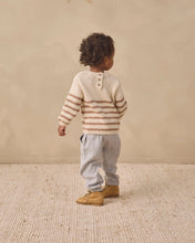 Load image into Gallery viewer, A toddler standing with their back to the camera, wearing a cream knit sweater with brown horizontal stripes, light gray pants, and tan boots, set against a neutral beige background.
