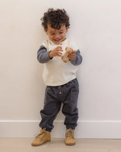 Load image into Gallery viewer, A toddler stands against a plain off-white wall wearing a cream and slate blue long-sleeve shirt, dark gray corduroy pants, and tan boots.
